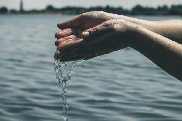 Cupped hands spill water in front of a lake.