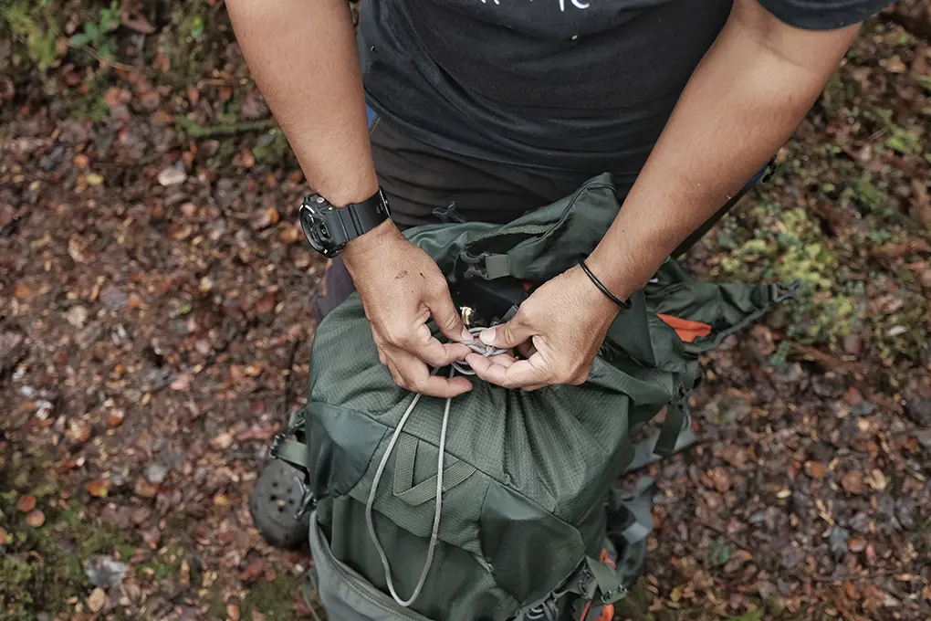 Person securing a green backpack in the forest, preparing for outdoor adventure or emergency