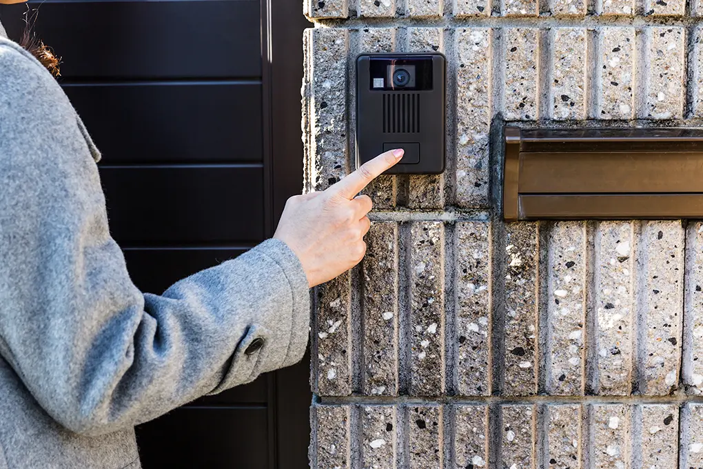 A hand pressing the button on a video doorbell installed outdoors