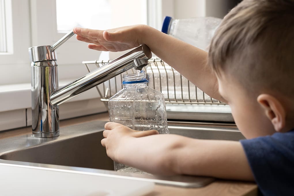 A child filling a clear water bottle from a sink