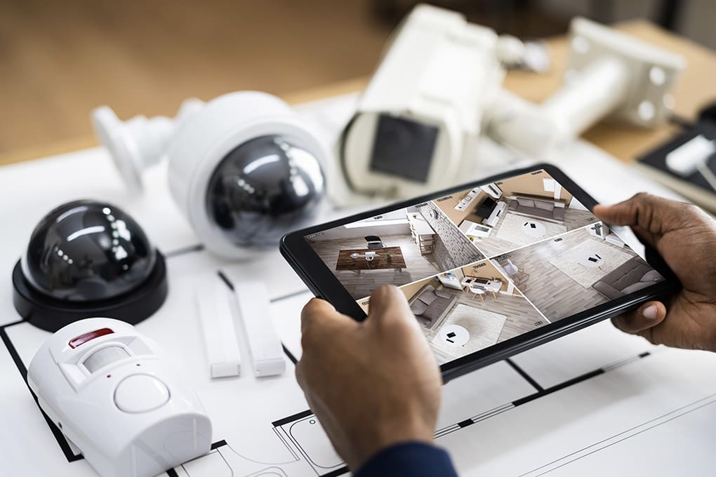 hands holding a screen tablet and home security cameras on a table.